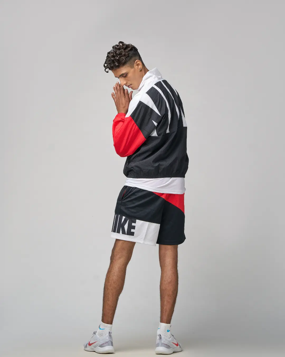 A dynamic menswear studio shot curated by a fashion stylist in Bangalore, showcasing a model in a bold red, black, and white Nike tracksuit and shorts ensemble.