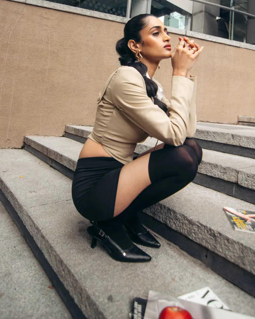A chic urban editorial curated by a fashion stylist in Bangalore, featuring a model in a beige cropped jacket, black mini skirt, and thigh-high stockings posing on stone steps.